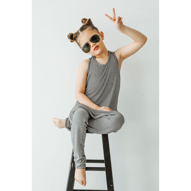 Child sitting on a stool wearing sunglasses and a gray outfit against a white background