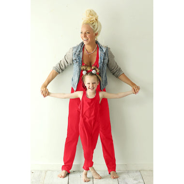 Woman and child in matching red outfits standing on a light wooden floor with a white background