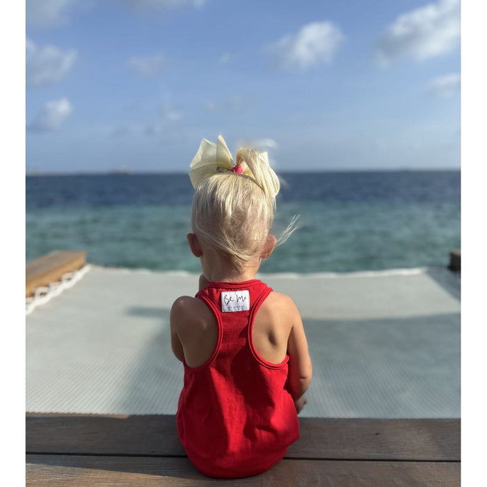 Child in a red dress sitting on a wooden bench overlooking the ocean.