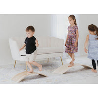Child balancing on a ShopMyLittleSongbird balance board rocker toy, featuring a colorful, curved wooden design for kids' play and activity.