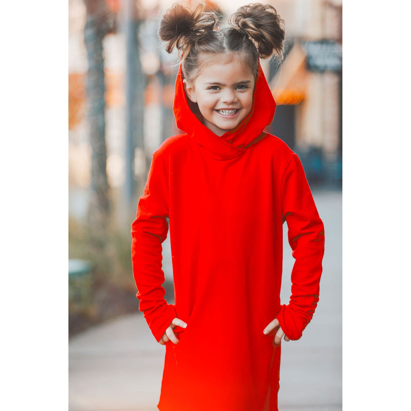 Girl in red hooded dress smiling over shoulder on sidewalk