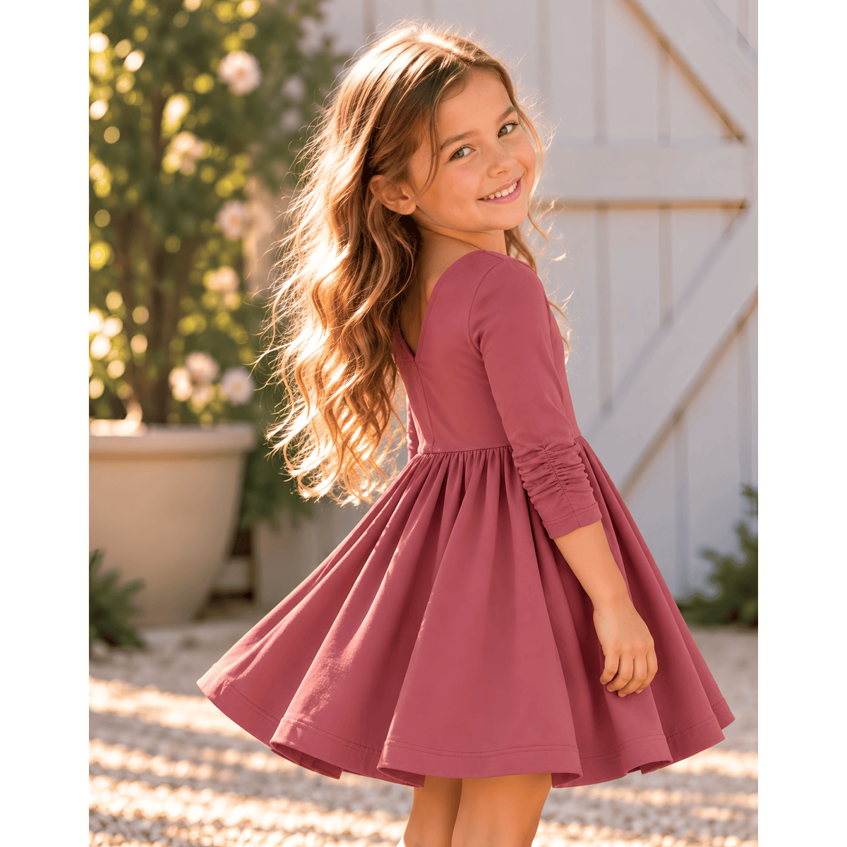 Girl wearing the Nova organic cotton twirl dress in muted berry, featuring a full circle skirt, round neckline, and delicate ruched sleeves.