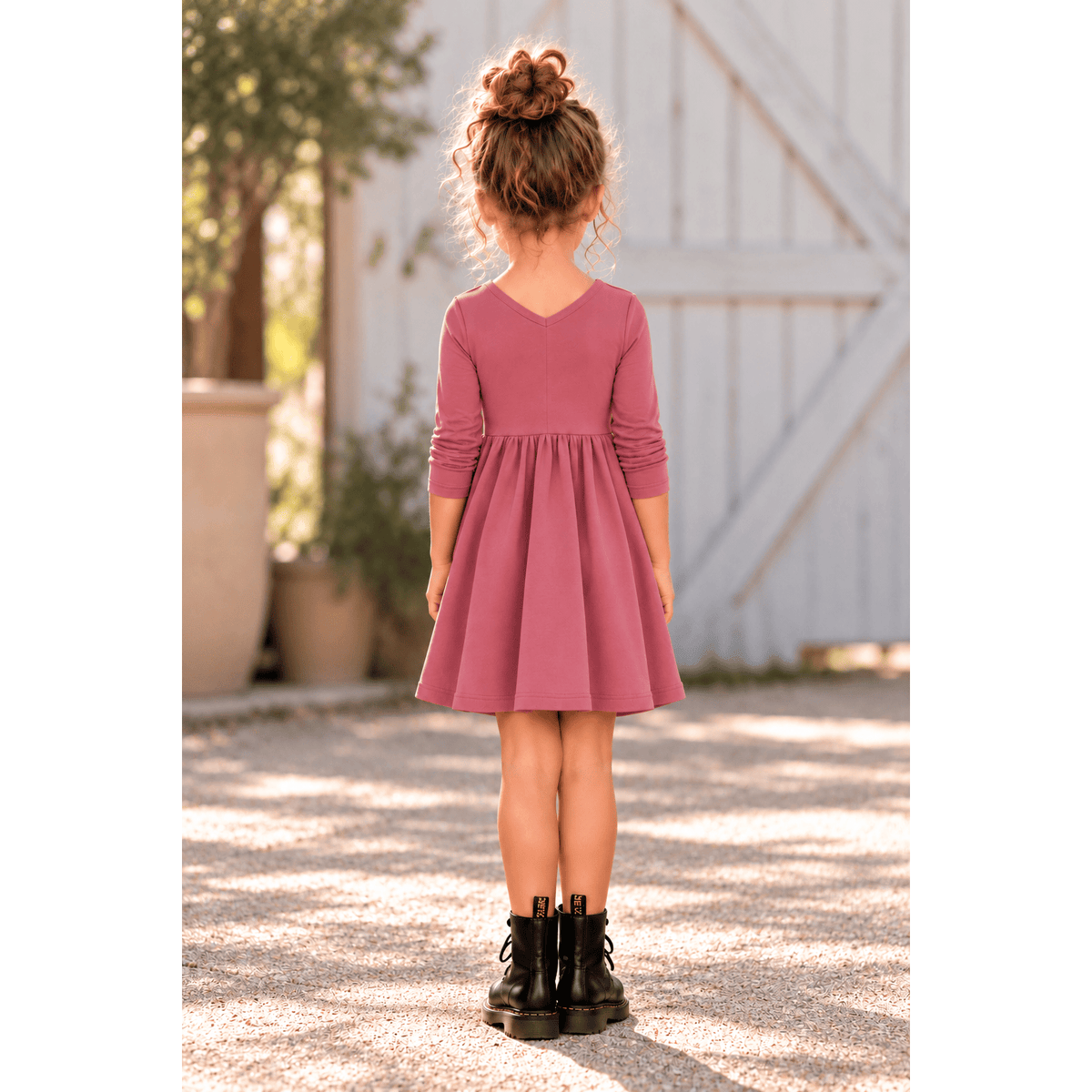 Girl wearing the Nova organic cotton twirl dress in muted berry, featuring a full circle skirt, round neckline, and delicate ruched sleeves.