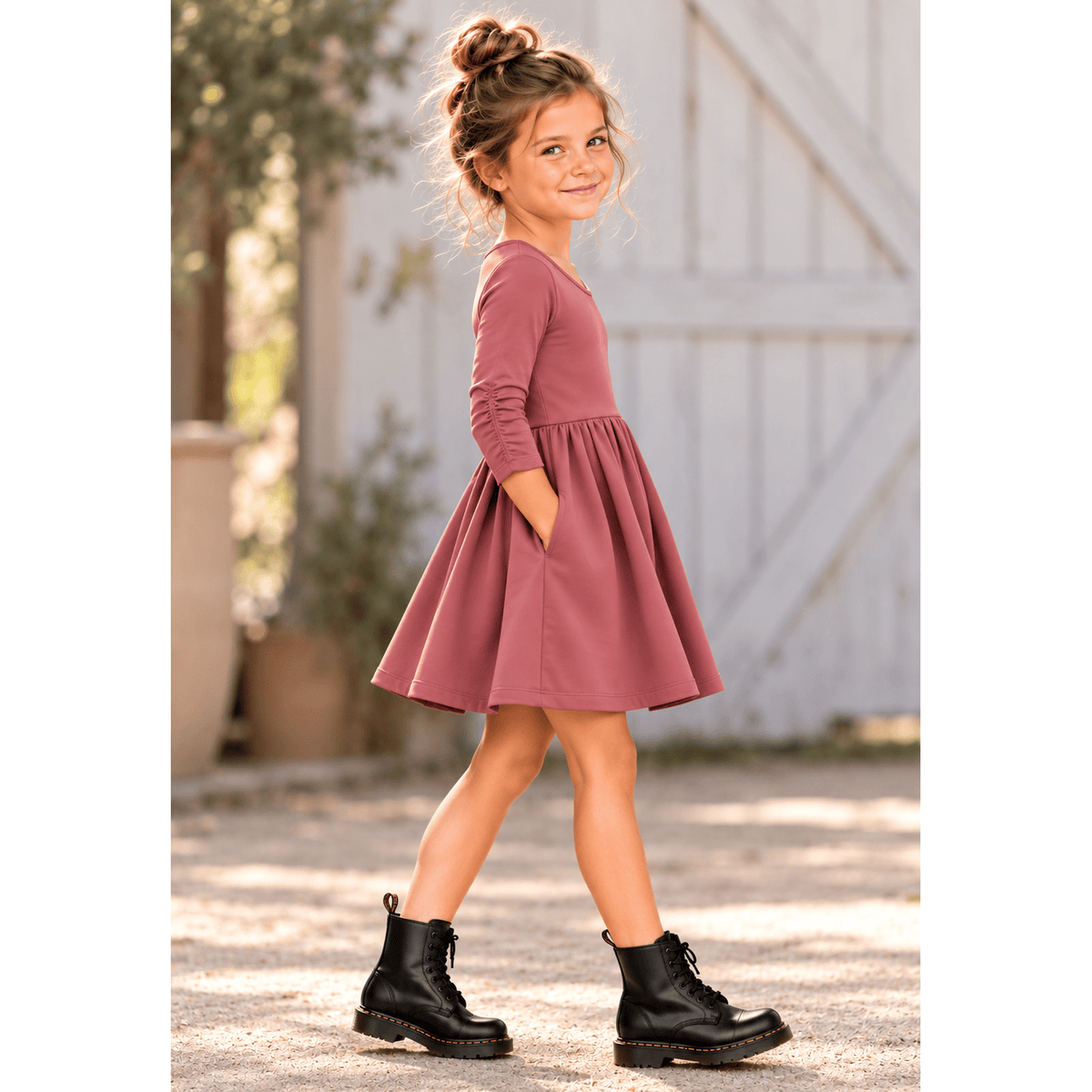 Girl wearing the Nova organic cotton twirl dress in muted berry, featuring a full circle skirt, round neckline, and delicate ruched sleeves.