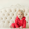 Baby in a red outfit sitting on a tufted headboard