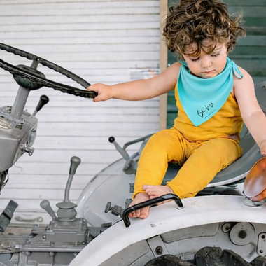 Child sitting on a tractor with a blue bandana and yellow romper