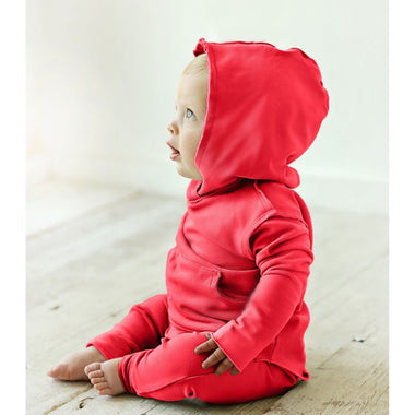 Baby wearing a red hoodie and pants sitting on a wooden floor.