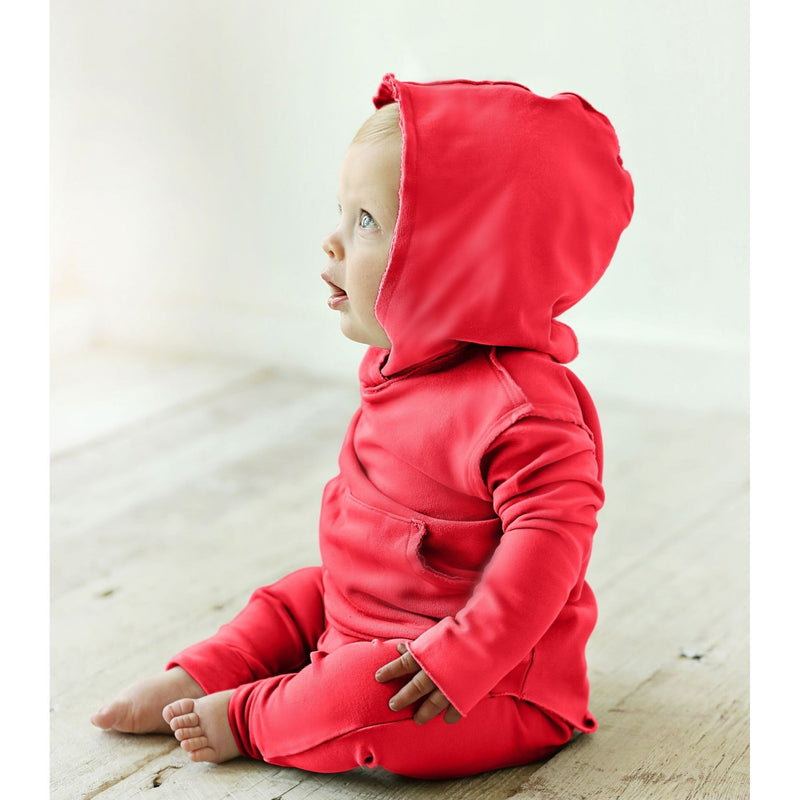 Baby wearing a red hoodie and pants sitting on a wooden floor.