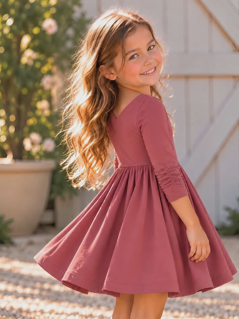 Girl wearing the Nova organic cotton twirl dress in muted berry, featuring a full circle skirt, round neckline, and delicate ruched sleeves.