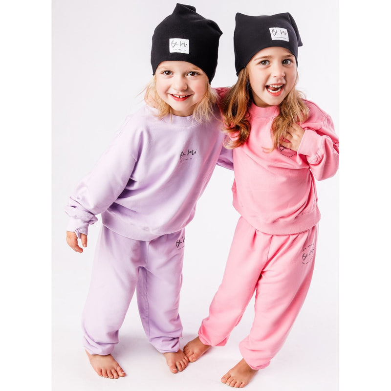 Two children wearing matching purple and pink outfits with black hats on a white background