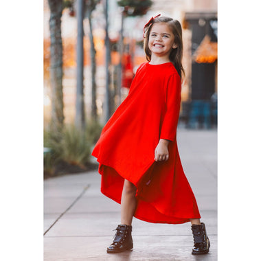 Young girl in a red dress standing on a sidewalk with blurred background