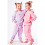 Two children wearing matching organic pink and lavender pajamas on a white background