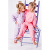 Two children in matching pink and purple outfits sitting on a chair.