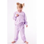 Child wearing a lavender organic sweatshirt and pants set on a white background