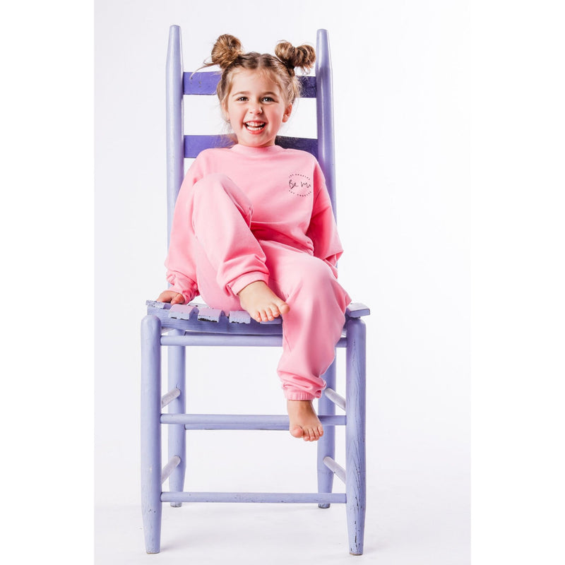 Child wearing pink pajamas sitting on a purple chair against a white background