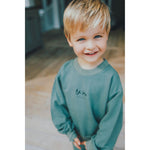 Child wearing a green sweatshirt with a logo indoors