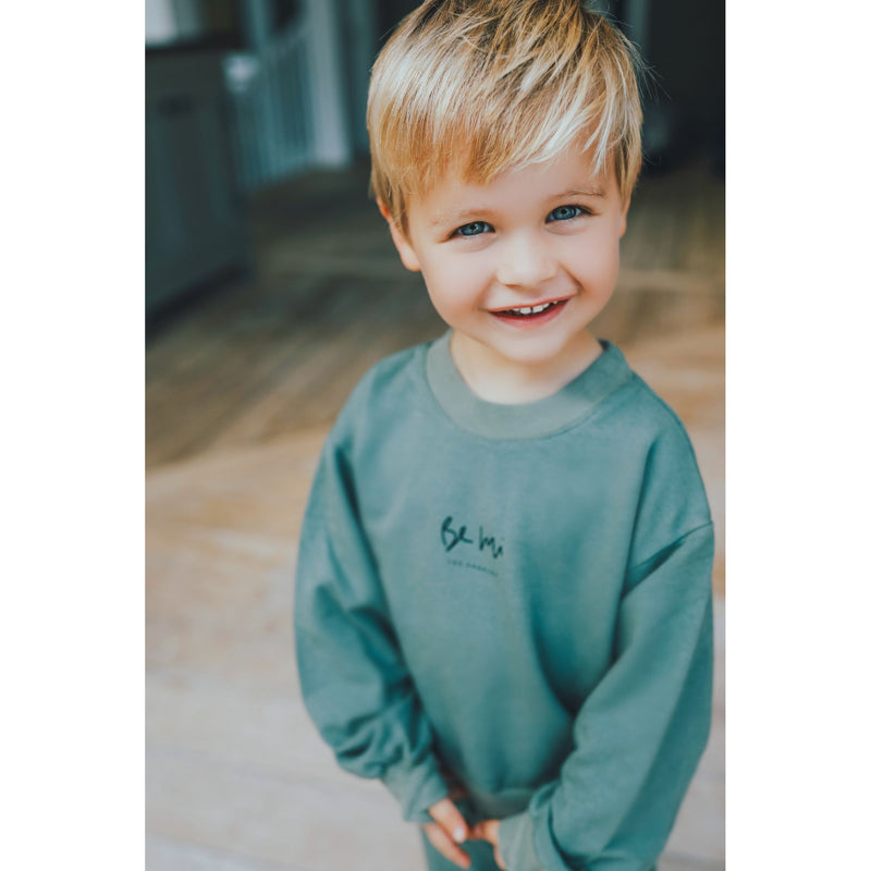 Child wearing a green sweatshirt with a logo indoors
