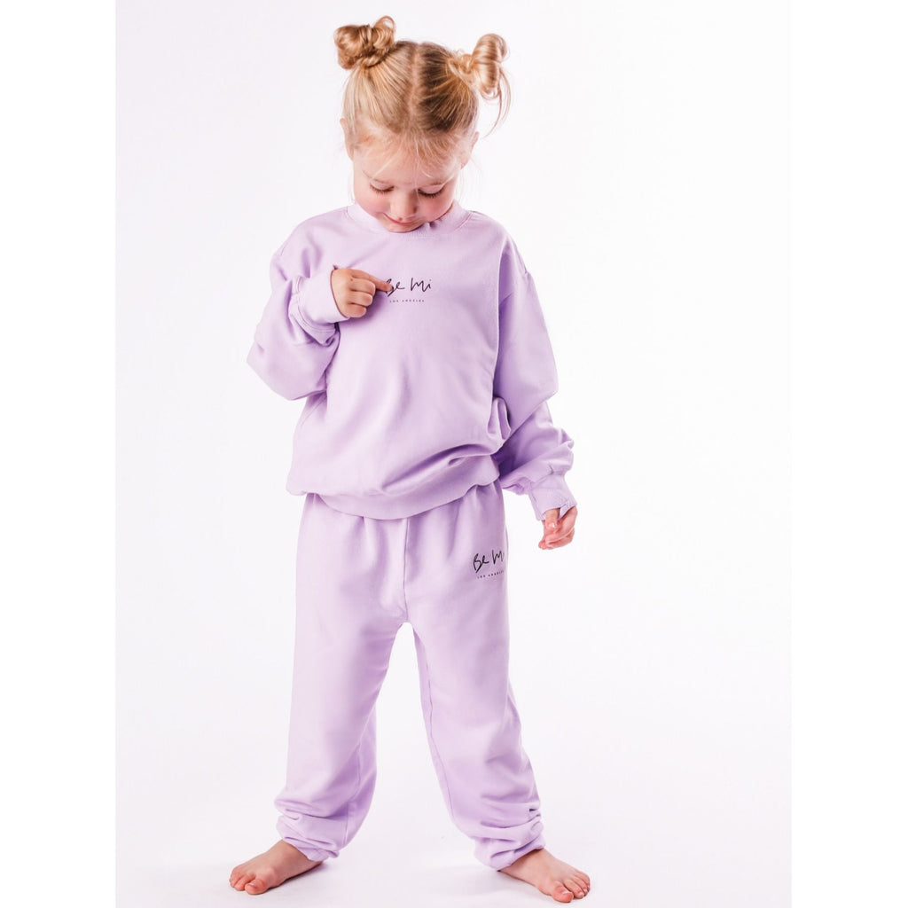 Child wearing a lavender sweatshirt and pants set on a white background