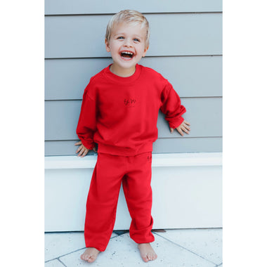 Child wearing a red outfit with a logo, standing against a light blue wall.