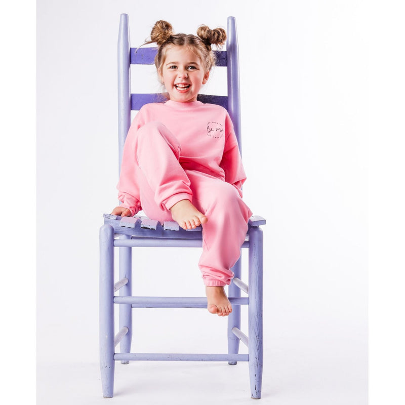 Child wearing pink pajamas sitting on a purple chair against a white background